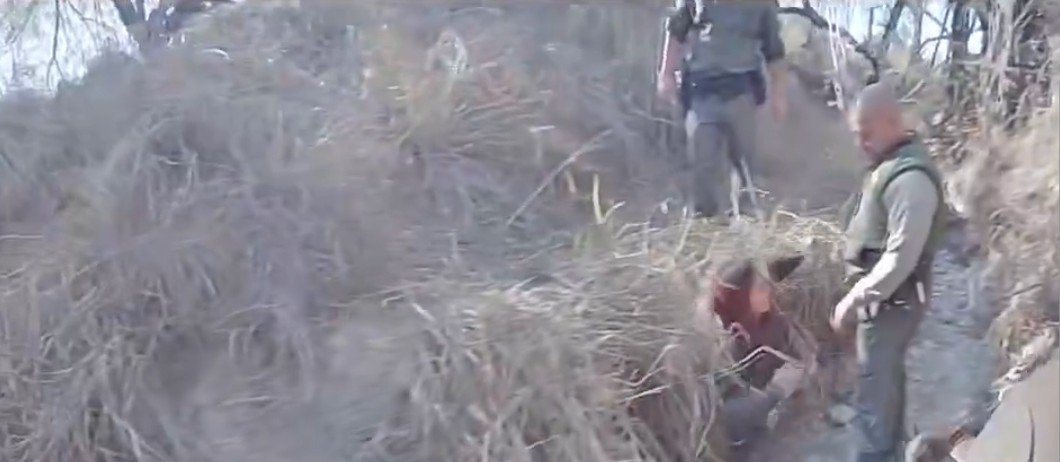Law enforcement officers assist an individual in dense grass during an outdoor operation.