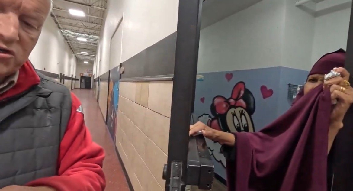 A man and a woman in a hallway discuss while a colorful mural featuring a cartoon character decorates the wall behind them.