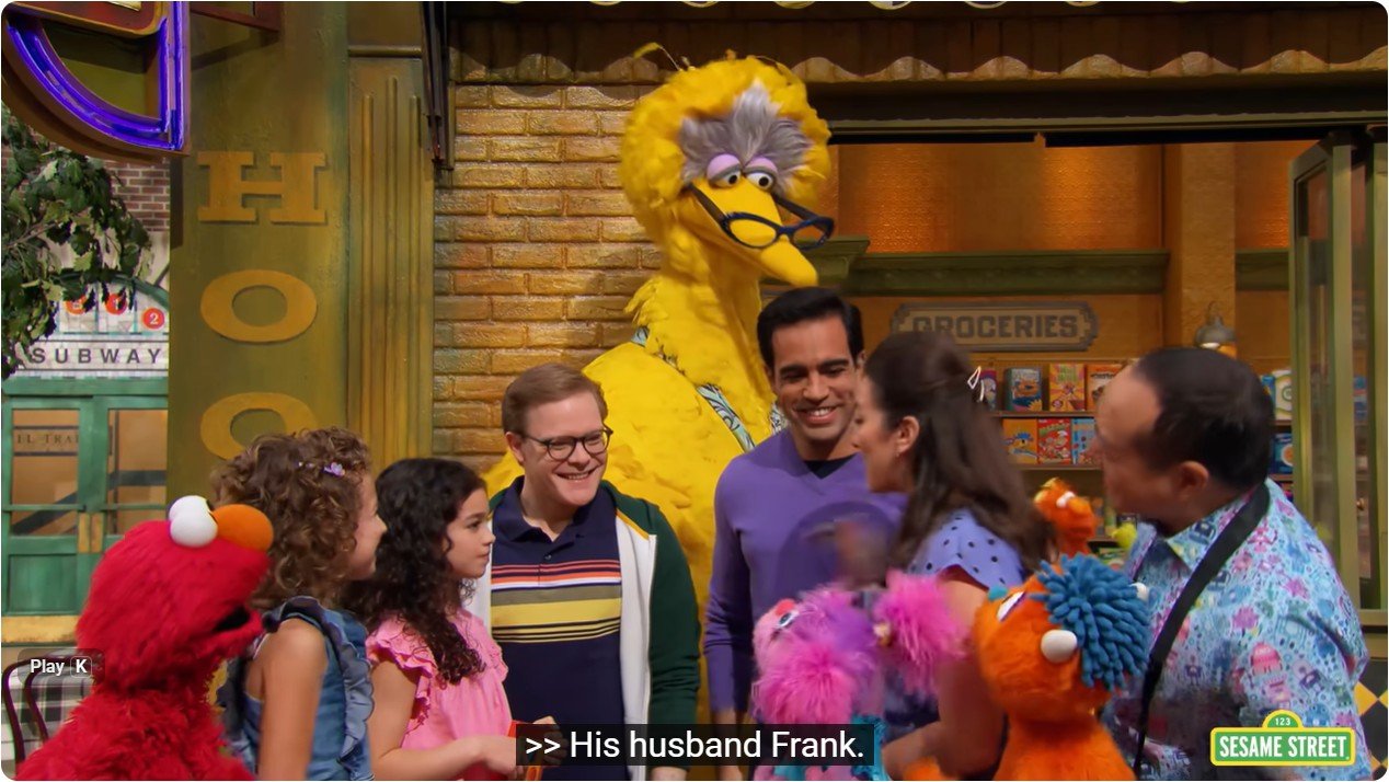 Children and adults gather on Sesame Street, featuring Big Bird and colorful characters, promoting friendship and inclusivity in a vibrant community setting.
