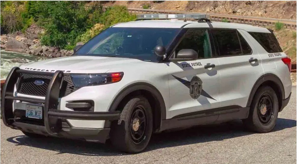 White Ford Interceptor SUV marked as State Patrol parked near a river, showcasing law enforcement presence in a scenic area.