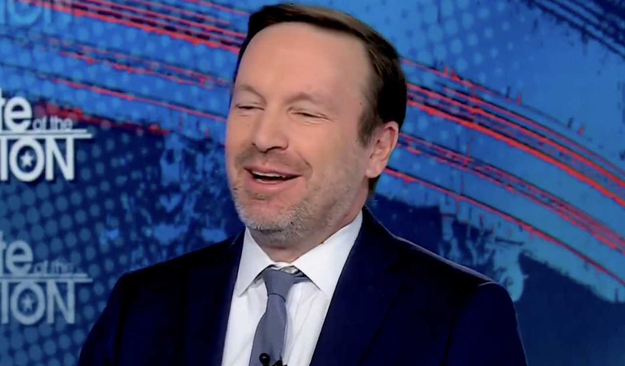 Smiling man in a suit discusses current events on a news program, with a colorful background featuring the show's title.