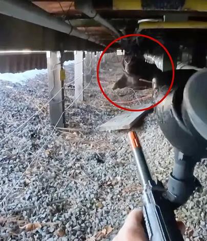 Person aiming a toy gun under a structure, with a small animal partially visible in the background among gravel and debris.