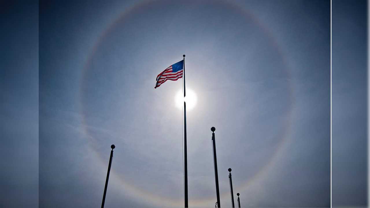 American flag waving under a sun halo against a clear sky, symbolizing patriotism and natural phenomena.