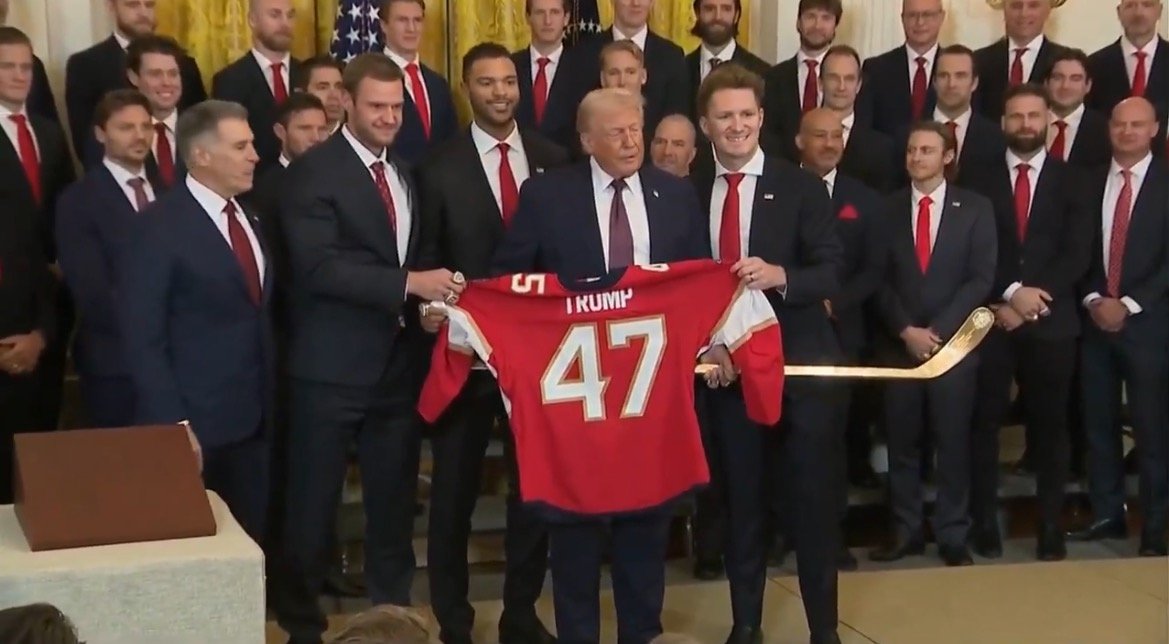 Donald Trump holds a hockey jersey with his name while posing with a group of players in formal attire during a ceremony at the White House.