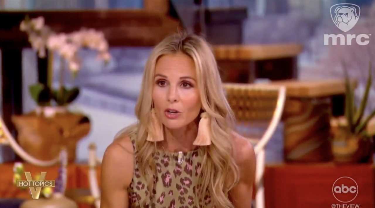 Television host passionately discussing current events on a talk show set, wearing a leopard print outfit and large earrings, with floral decor in the background.