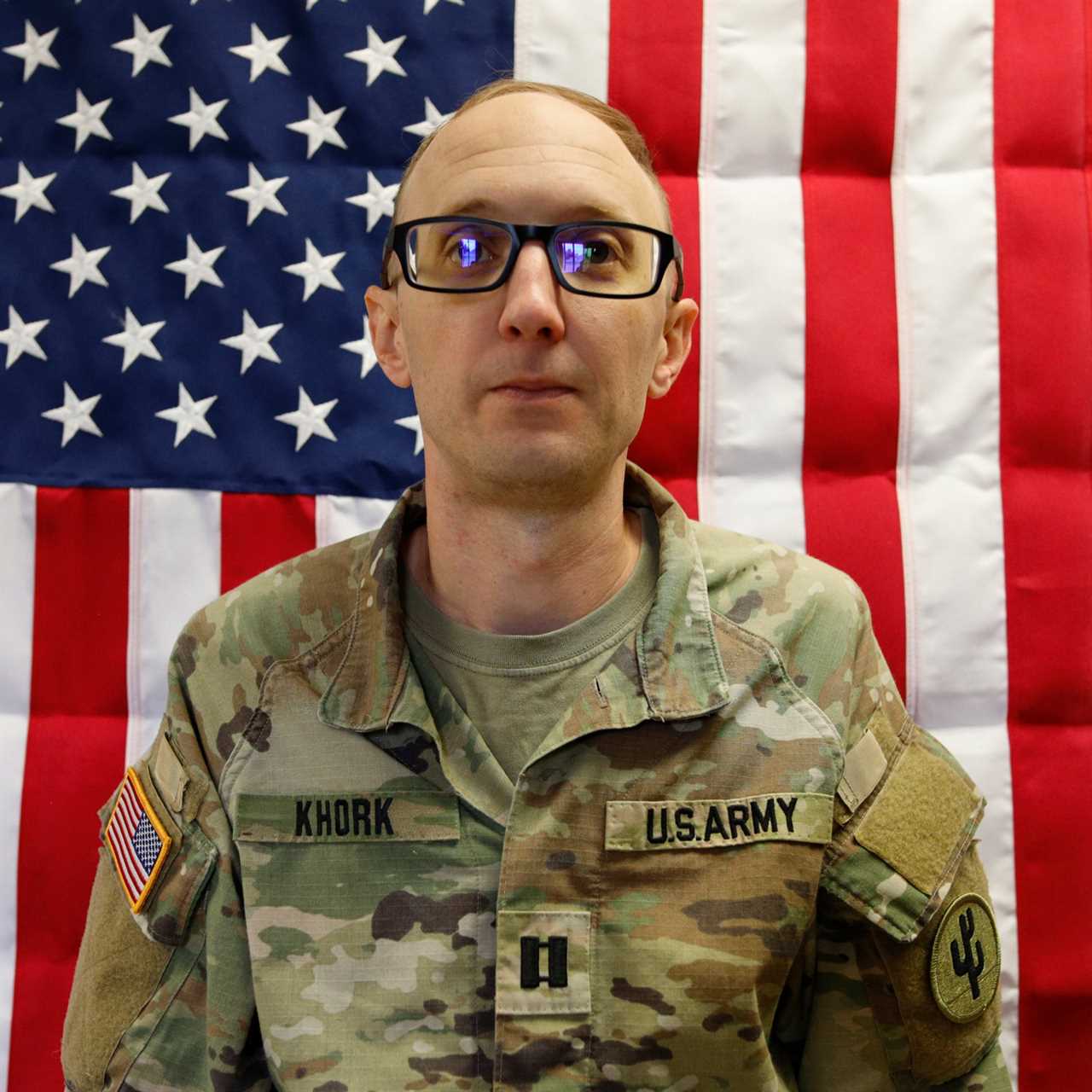 U.S. Army soldier in uniform standing in front of an American flag, showcasing military service and patriotism.