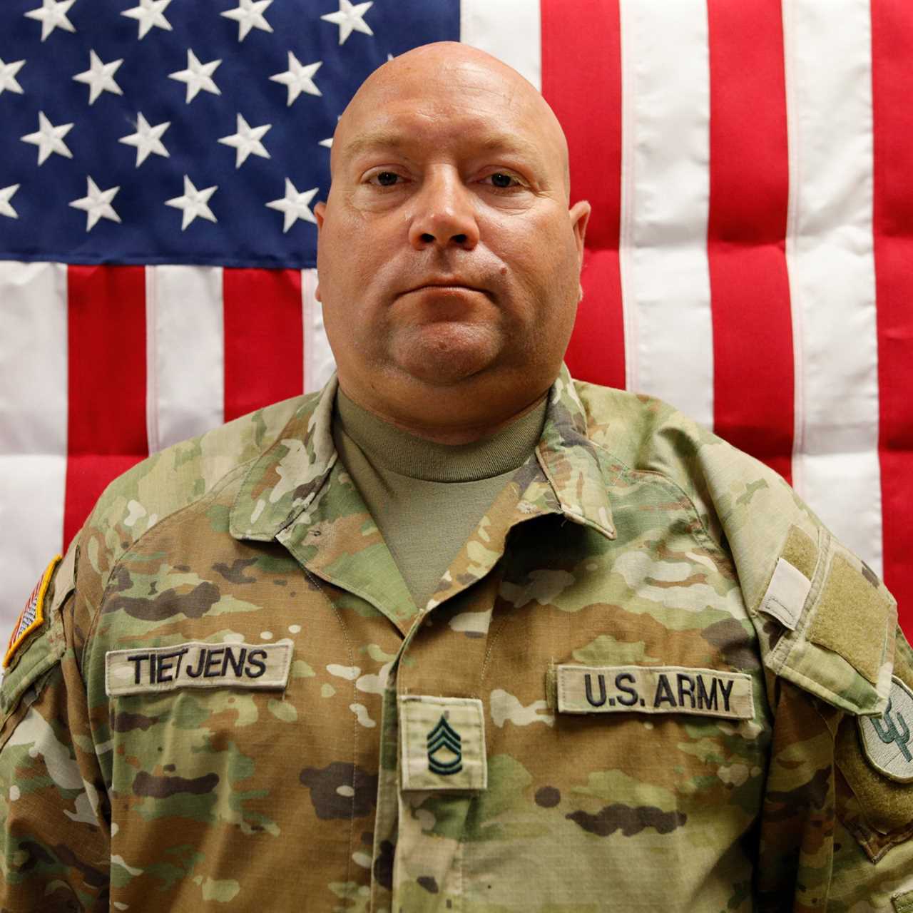 U.S. Army soldier Tietjens poses in front of an American flag, showcasing military attire and rank insignia.