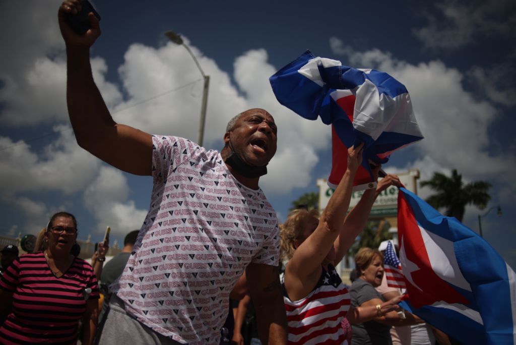 Demonstrators passionately wave flags and chant during a rally, showcasing support for Cuban freedom and expressing solidarity in a vibrant public space.