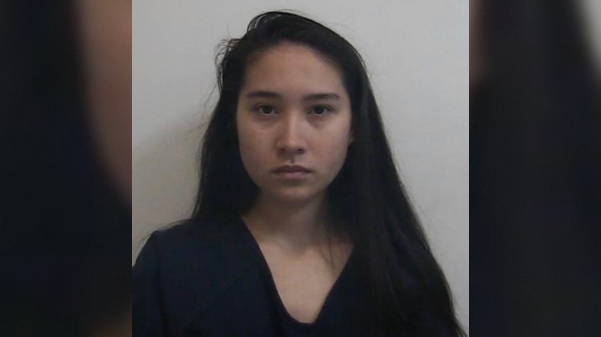 Mugshot of a young woman with long black hair, wearing a dark outfit, against a plain background.