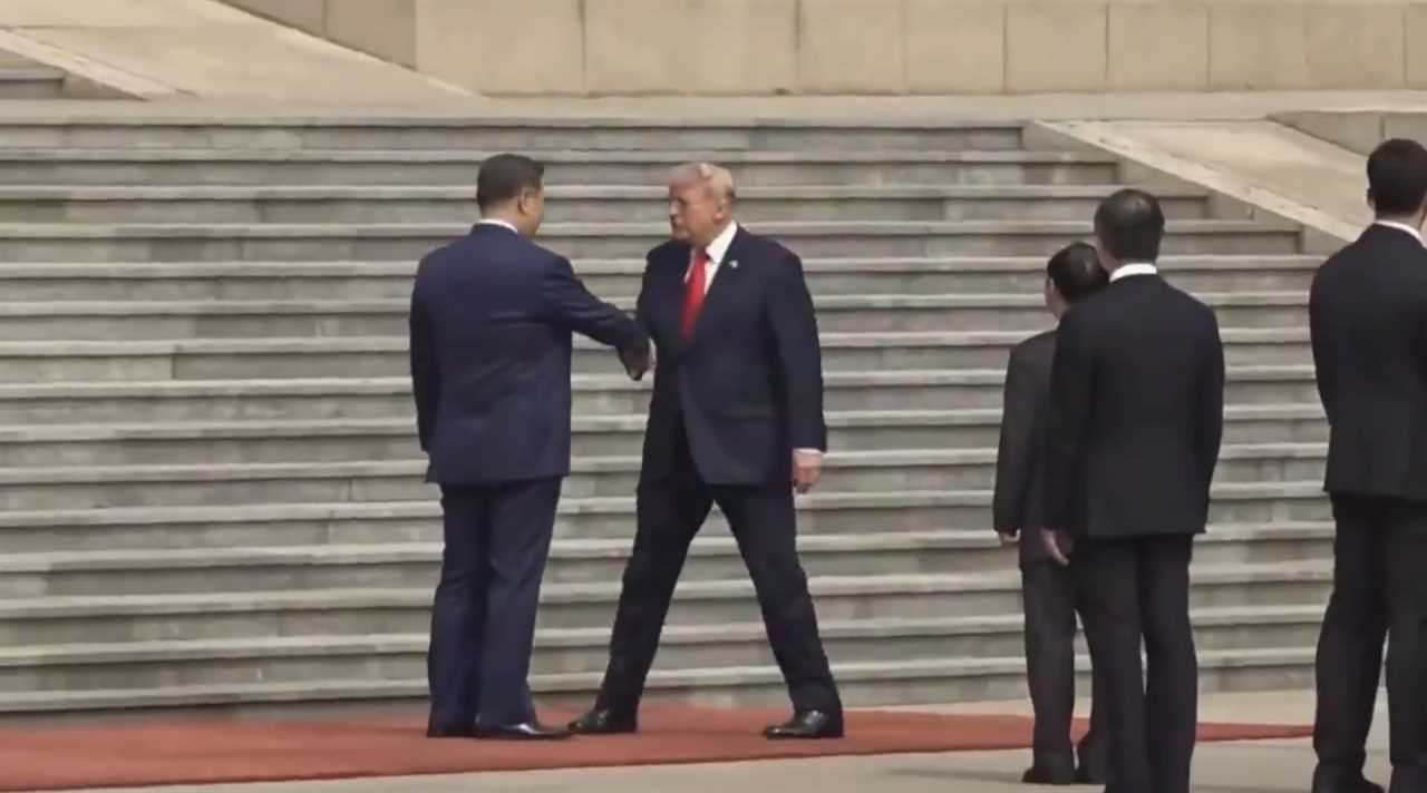 World leaders Xi Jinping and Donald Trump shake hands on steps during a formal meeting, surrounded by security personnel.