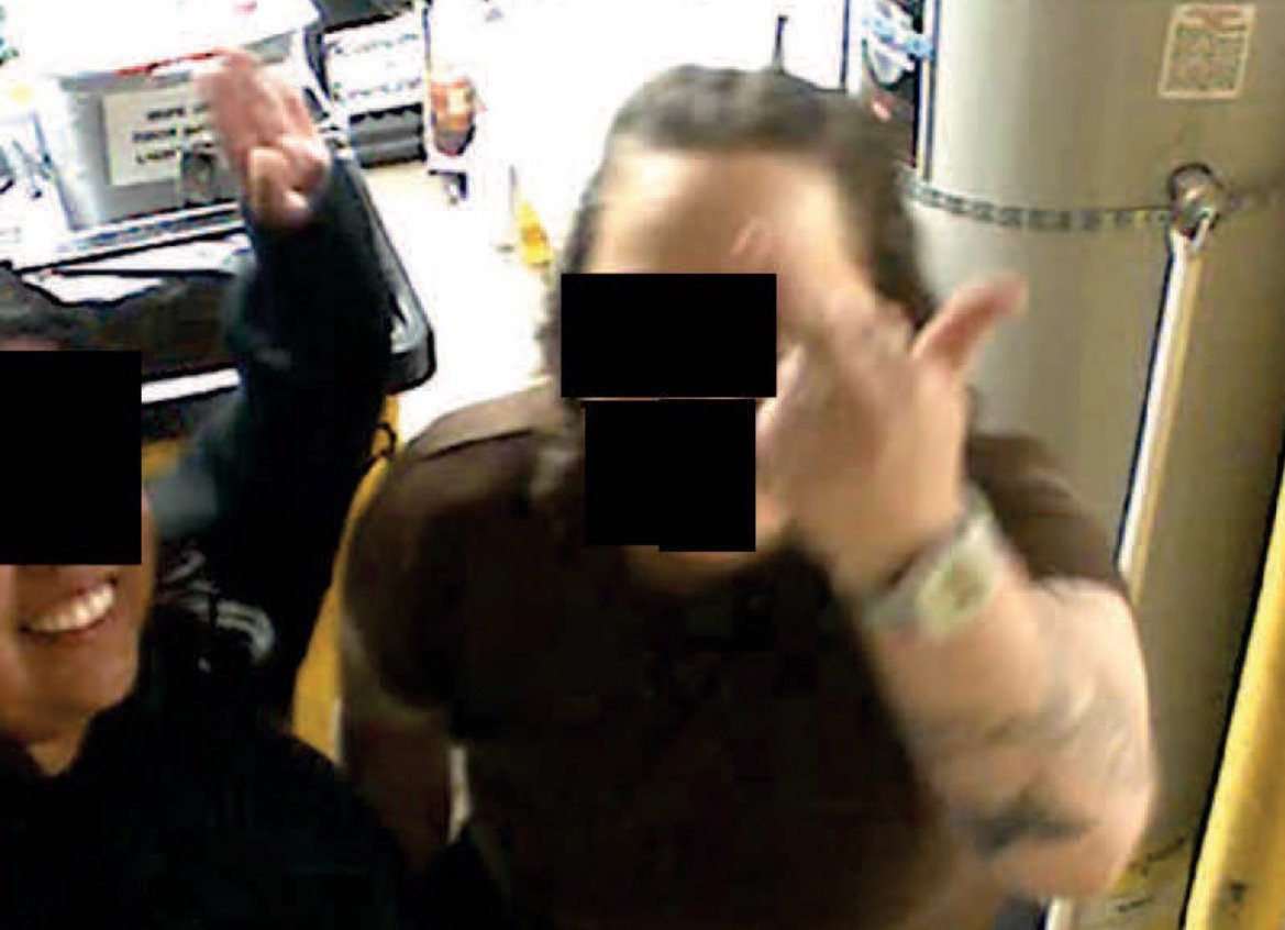 Two individuals posing playfully in a kitchen, one making a hand gesture while the other smiles, with blurred faces for privacy.