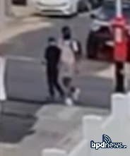 Two individuals walking on a city street near parked cars and a fire hydrant.