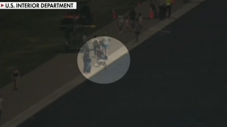Aerial view of individuals near a water body, with safety cones and personnel visible, highlighting a public event organized by the U.S. Interior Department.